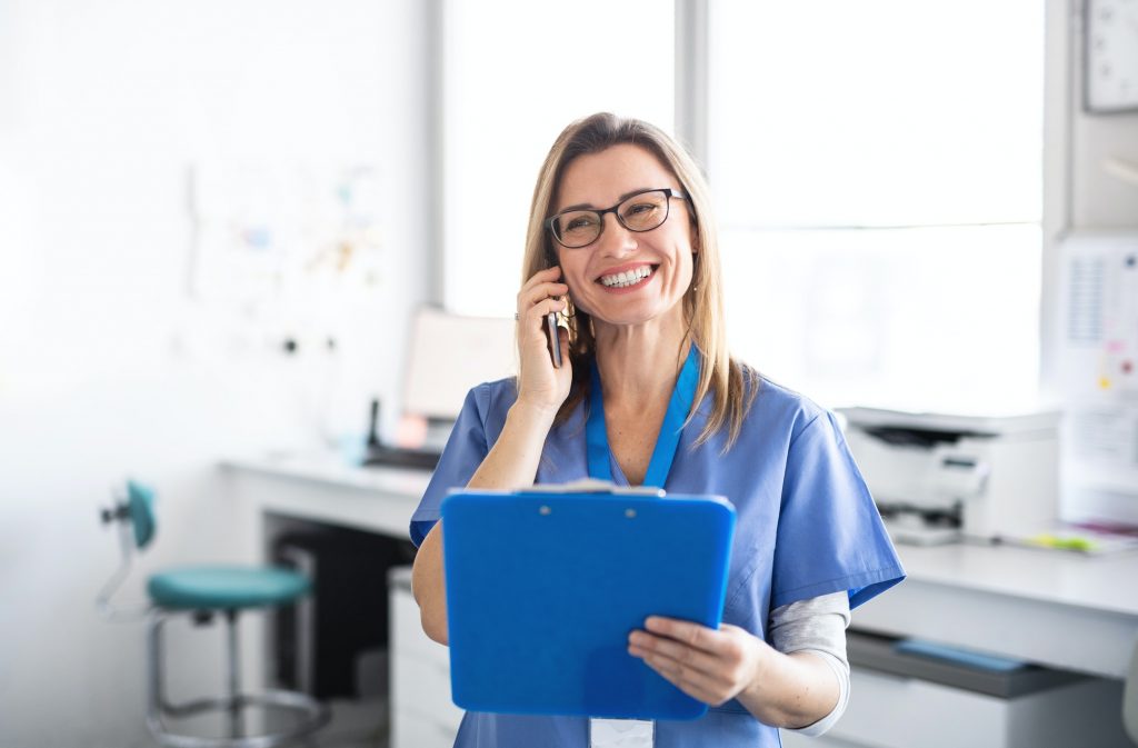 A portrait of dental assistant in modern dental surgery, using smartphone