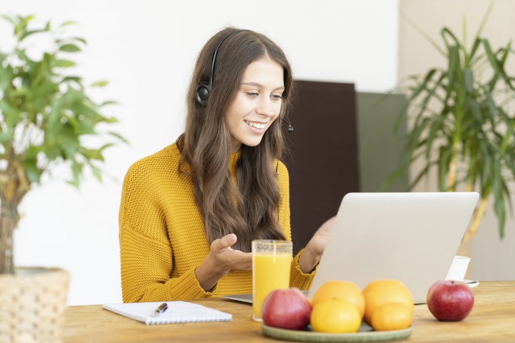 Happy woman in headset speaking by conference call and video chat on laptop in office. Online