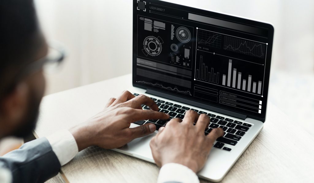 Black Businessman Working On Laptop With Graphs Sitting In Office